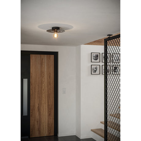 Karnette Wall Light in black and light grey, shown mounted on a hallway ceiling with a round black base, disc-shaped glass shade, and exposed bulb.