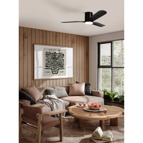 Kawana Ceiling Fan with Light in matt black, three curved blades and integrated round LED shade, shown low-profile on the ceiling of a living room with wood panelling and a neutral sofa.