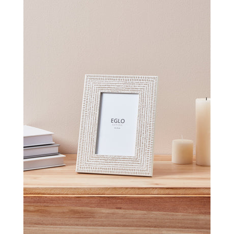 Kemayan Photo Frame with cream border and taupe dashed pattern, displayed on a wooden surface beside stacked books and candles.