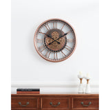 Kenema Wall Clock 53.5cm in antique copper, round skeleton frame with Roman numerals and exposed gear centre, shown above a wooden sideboard with candlesticks and books.