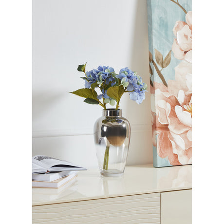 Kenyasi Glass Vase 32.5cm with mirrored silver top fading to clear glass, holding blue hydrangea stems on a cabinet beside a floral canvas print.