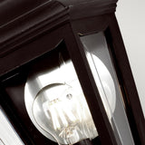 Close-up of the Kerry 1 Light Outdoor Flush Wall Light in black, featuring a clear glass pane that reveals a glowing bulb inside. The sleek metal frame flaunts a modern design, IP44 rating, and corrosion-proof features, softly illuminating its surroundings.