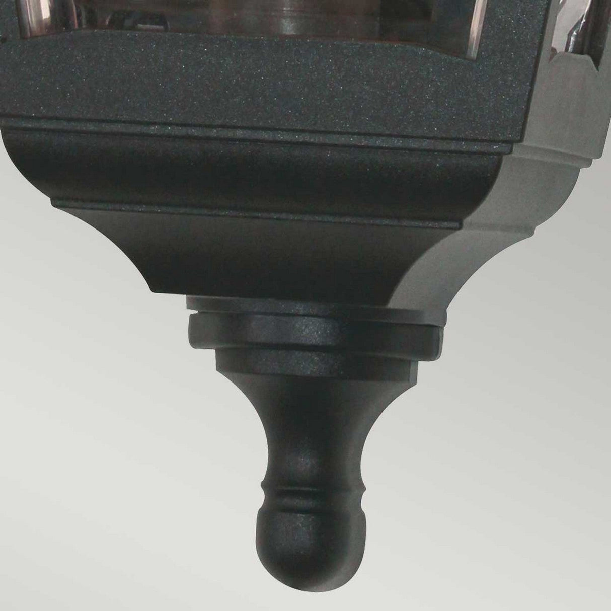 Close-up of the Kerry 1 Light Outdoor Flush Wall Light in black, designed to be corrosion-proof and boasting an IP44 rating. It showcases a decorative finial and modern, minimalist design with a rectangular shape and slightly reflective surfaces, set against a light gray background.