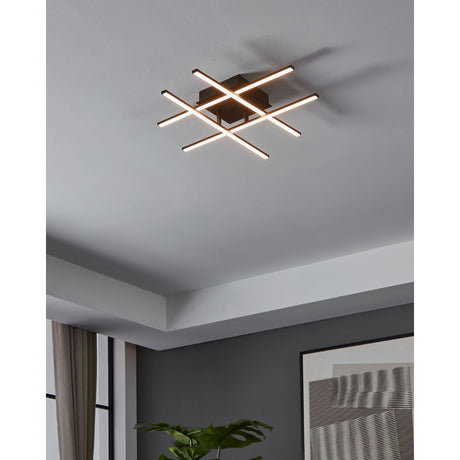 Keselle LED 4 Light Flush Ceiling Light in black, four slim crossed LED bars glowing warm white on a square black base, shown mounted on a grey hallway ceiling.
