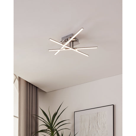 Keselle LED flush ceiling light in chrome, three crossed slim bars with white diffusers fitted to a ceiling, shown in a room with curtains, plant and framed artwork below.