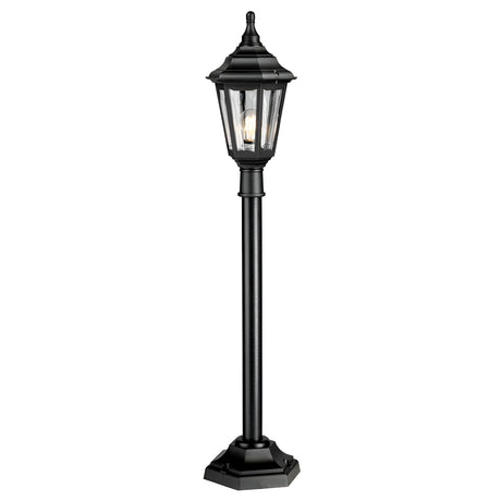 The Kinsale 1 Light Pillar Light - Black is an outdoor post light with a lantern-style design featuring a hexagonal base and clear glass panels. It showcases a decorative, traditional look with a pointed top that reveals the bulb inside, providing corrosion resistance for enduring outdoor elegance.