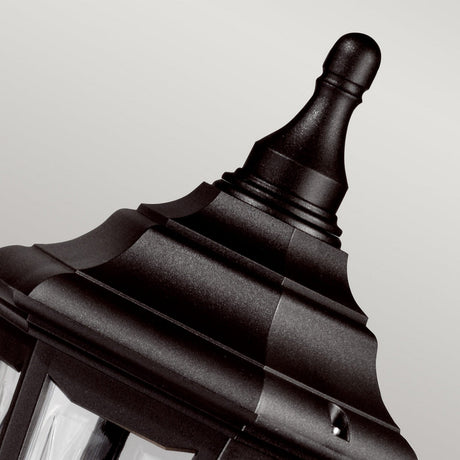 A close-up of the Kinsale 1 Light Pillar Light in black showcases its decorative top against a light gray background. This outdoor lantern features an elegant pointed finial and a classic, textured design with smooth and ridged sections, providing both style and corrosion resistance.
