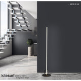 A modern minimalist room features a floating staircase, large windows, and the Kitesurf LED Floor Lamp 24W 3000K - Black against a dark wall. The text reads, ... siente la luz, and kitesurf series by mantra.