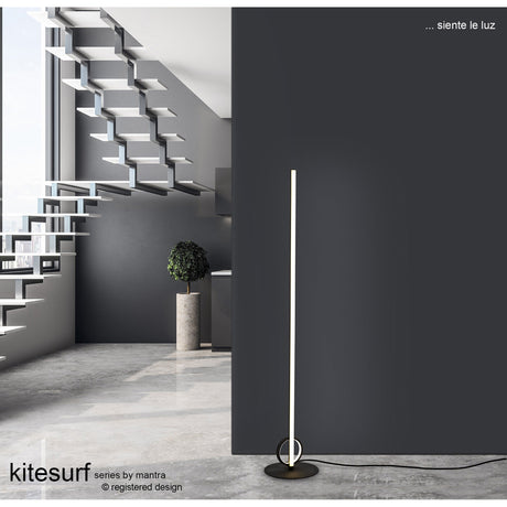 A modern minimalist room features a floating staircase, large windows, and the Kitesurf LED Floor Lamp 24W 3000K - Black against a dark wall. The text reads, ... siente la luz, and kitesurf series by mantra.