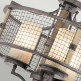 A close-up of the Ahrendale 3 Light Duo-Mount Chandelier - Grey highlights its industrial-style charm with a metal cage accentuating rustic elegance alongside three cylindrical frosted glass shades. The design seamlessly incorporates modern elements, including a Vetro Mica grid pattern and a textured metal finish reminiscent of this distinctive chandelier.