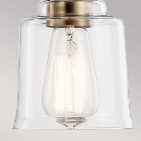 A close-up of the Aivian 1 Light Pendant showcases its modern design, featuring a clear glass shade and an exposed filament bulb against a plain gray background. The weathered brass fitting contributes an industrial-inspired touch to this sophisticated piece.