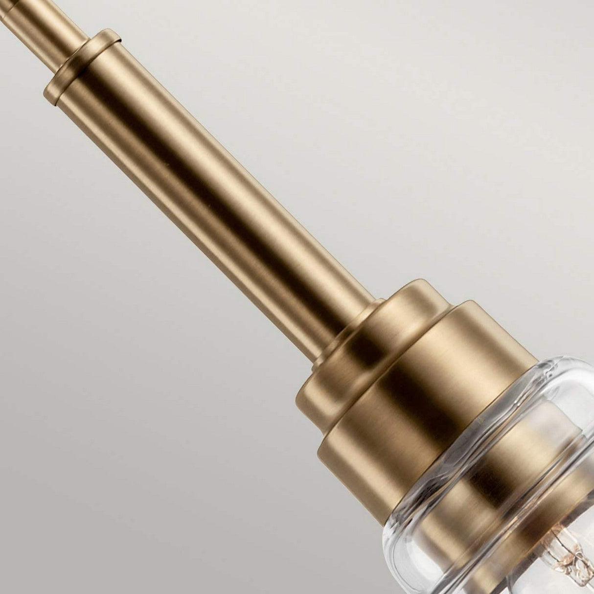 A close-up of the Aivian 1 Light Pendant in weathered brass, featuring a sleek modern design with a clear glass shade, set against a neutral background.