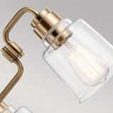Close-up of the Aivian 3 Light Chandelier in weathered brass, highlighting its industrial aesthetics with a transparent glass shade that showcases exposed light bulbs. The sleek, curved design contrasts elegantly against a neutral gray background.