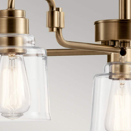 A close-up of the Aivian 5 Light Chandelier - Weathered Brass showcases its weathered brass fixtures and transparent glass bulb covers. The exposed light bulbs emphasize its sleek, industrial style design set against a neutral background.