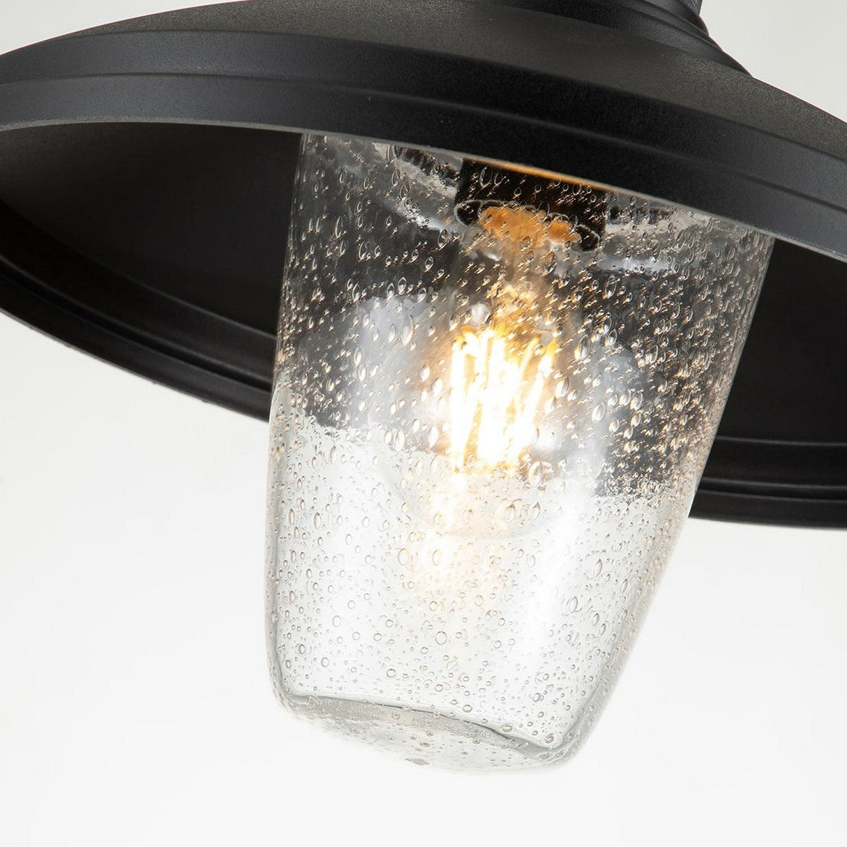 A close-up of the black metal Allenbury Outdoor 1 Light Pendant showcases its Textured Black finish and clear glass shade, revealing a lit bulb inside. This weather-resistant fixture features a bubbled design that adds a decorative touch.