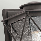 Close-up of the Argyle Outdoor 1 Light Small Wall Light - Weathered Zinc, mounted on a wall. This black outdoor lantern features seeded glass panels with raindrop details and an internal light bulb, all enhanced by decorative crisscross metal bars.