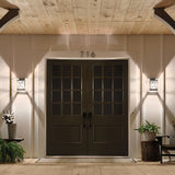 A large double door entrance painted dark with seeded glass panels is flanked by Argyle Outdoor 1 Light Small Wall Lights in weathered zinc. The house number 716 is positioned above the doors. A small plant and tree stump seat are placed on either side, all under a wooden ceiling finished in weathered zinc.