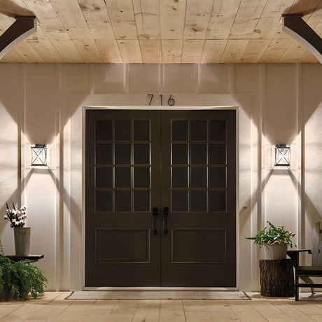 A large double door entrance painted dark with seeded glass panels is flanked by Argyle Outdoor 1 Light Small Wall Lights in weathered zinc. The house number 716 is positioned above the doors. A small plant and tree stump seat are placed on either side, all under a wooden ceiling finished in weathered zinc.