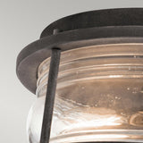 Close-up of the Ashland Bay Outdoor 2 Light Outdoor Ceiling Flush in weathered zinc, showcasing a black metal and glass lantern with a circular design. The ribbed texture of the clear seeded glass encases the light bulb, exuding an elegant ambiance. This modern fixture is set against a plain gray background.