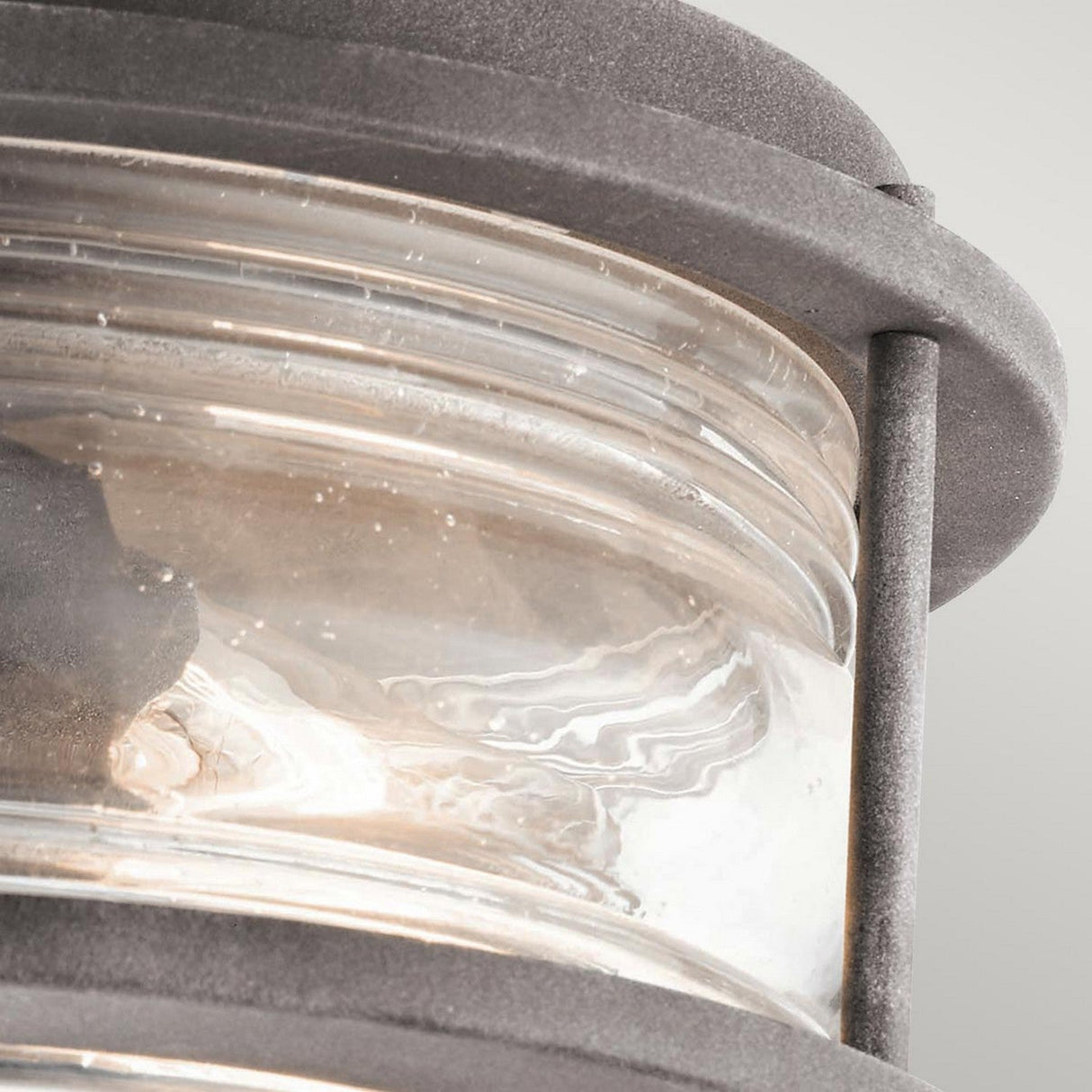 Close-up of the Ashland Bay Outdoor 2 Light Ceiling Flush in a weathered zinc finish. The clear seeded glass, which is ribbed and slightly frosted, showcases a visible bulb, giving the fixture a classic and sturdy look.