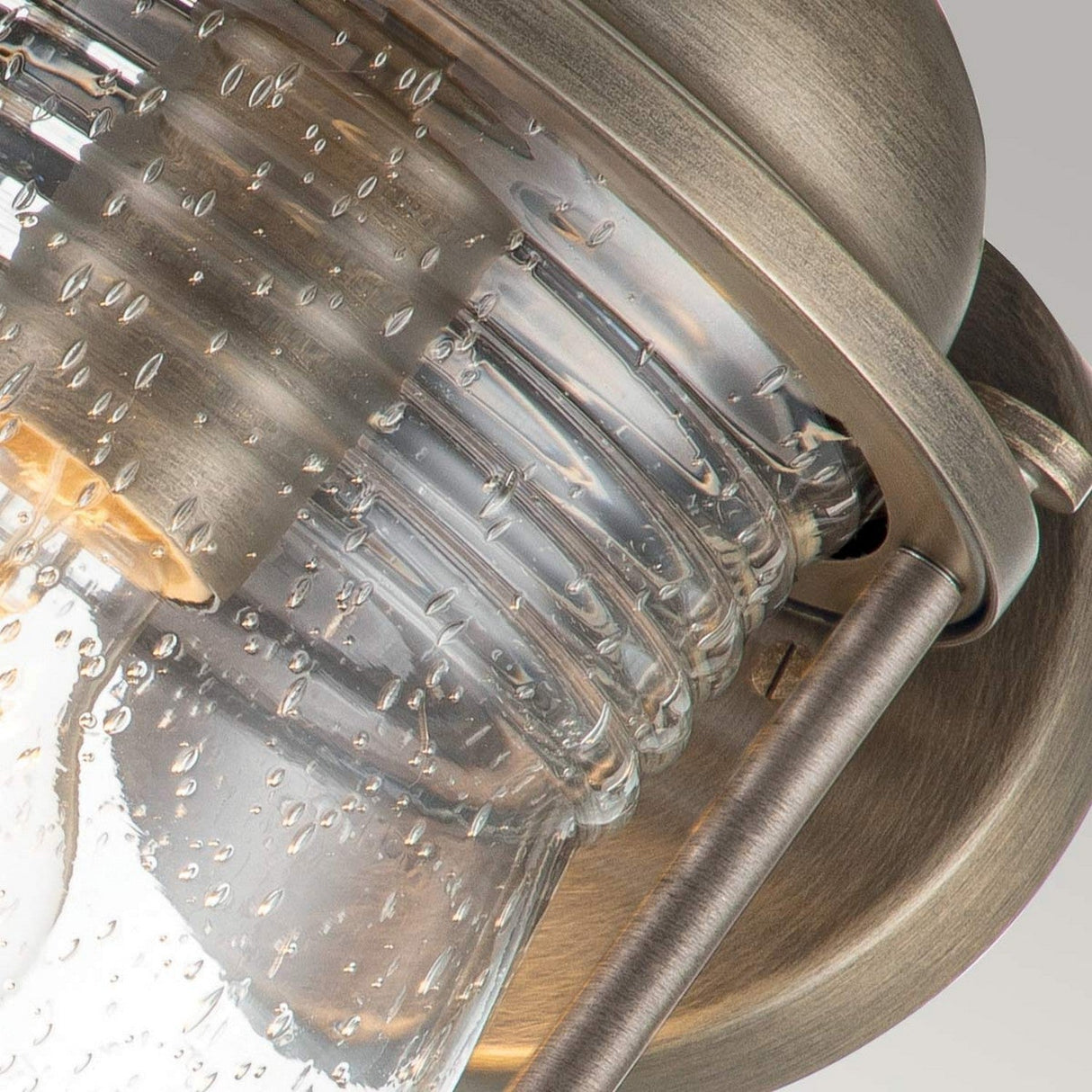 Close-up of the Ashland Bay Outdoor 1 Light Medium Wall Lantern showcasing its vintage-style design with a burnished bronze metal frame and clear seeded glass cover featuring small air bubbles. The fixture's weathered, antique finish contributes to its rustic appearance against a neutral background.