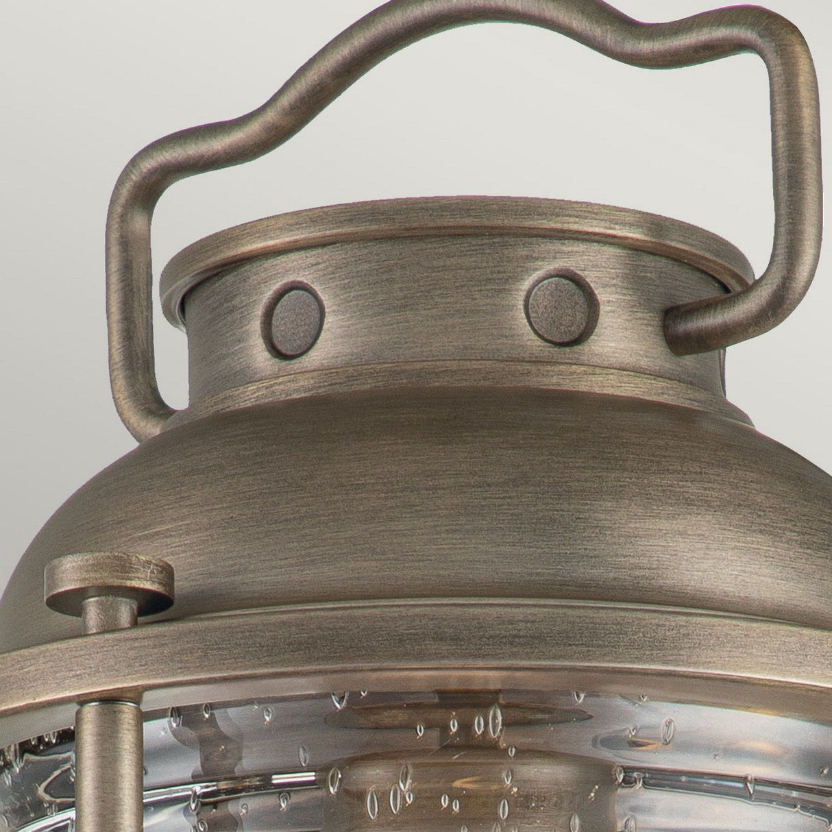 Close-up of the Ashland Bay Outdoor 1 Light Medium Wall Lantern in burnished bronze, showcasing its rustic finish with large circular rivets and a curved handle. The clear seeded glass detailing, adorned with small bubble-like patterns, enhances its vintage aesthetic as an elegant outdoor wall lantern.