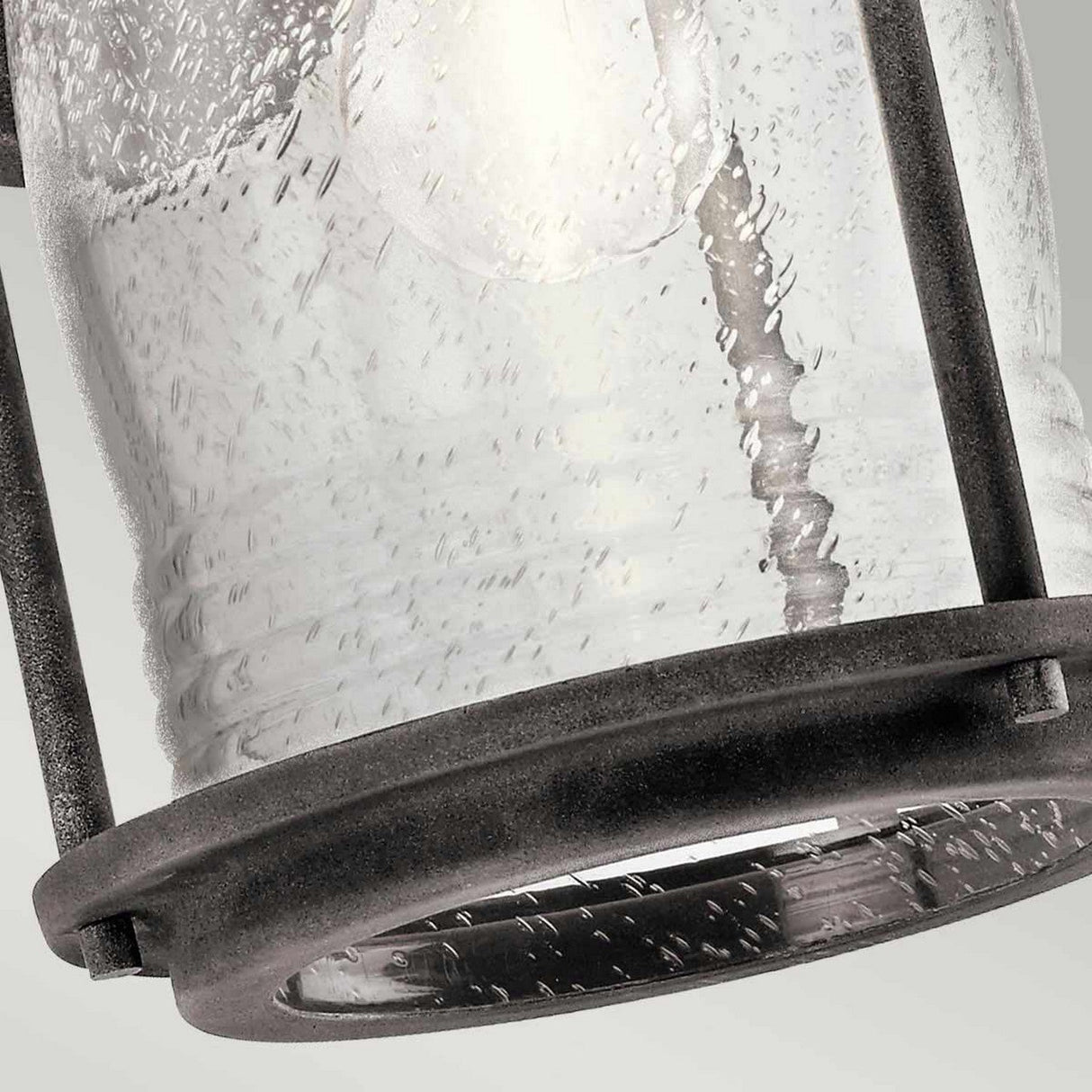 Close-up of the Ashland Bay Outdoor 1 Light Medium Wall Lantern - Weathered Zinc, showcasing its seeded glass with visible water droplets. The lantern has weathered zinc frames and appears to hang at a slight angle against a light gray background, with the glass exhibiting a slightly textured surface.