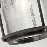 Close-up of the Ashland Bay Outdoor 1 Light Medium Wall Lantern - Weathered Zinc, showcasing its seeded glass with visible water droplets. The lantern has weathered zinc frames and appears to hang at a slight angle against a light gray background, with the glass exhibiting a slightly textured surface.