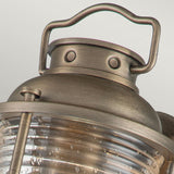 Close-up of the Ashland Bay Outdoor 1 Light Small Wall Lantern in burnished bronze. The top section showcases a handle and rivet details, while the lower part features ribbed glass housing LED Edison bulbs, creating a warm and inviting glow.