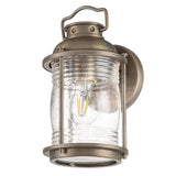 Introducing the Ashland Bay Outdoor 1 Light Small Wall Lantern in Burnished Bronze, which elegantly combines vintage charm with modern design. This wall lantern showcases a clear glass encasement that highlights a visible LED Edison bulb, all mounted thoughtfully on a round base with an appealing handle-like accent on top.