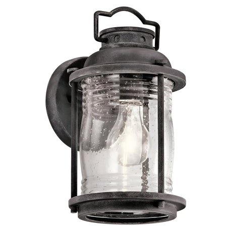 The Ashland Bay Outdoor 1 Light Small Wall Lantern in weathered zinc showcases a colonial design with clear glass panels and a visible light bulb. It features a robust metal frame and includes a looped handle on top for hanging, offering timeless elegance.