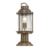 The Ashland Bay Outdoor 1 Light Medium Pedestal Lantern in burnished bronze features a vintage-style design with a clear glass enclosure that highlights a visible LED Edison bulb. It includes a handle on top and has a round base for stability, making it perfect for outdoor use.