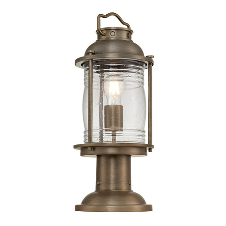 The Ashland Bay Outdoor 1 Light Medium Pedestal Lantern in burnished bronze features a vintage-style design with a clear glass enclosure that highlights a visible LED Edison bulb. It includes a handle on top and has a round base for stability, making it perfect for outdoor use.