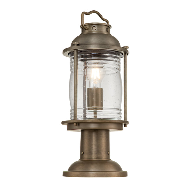 The Ashland Bay Outdoor 1 Light Medium Pedestal Lantern in burnished bronze features a vintage-style design with a clear glass enclosure that highlights a visible LED Edison bulb. It includes a handle on top and has a round base for stability, making it perfect for outdoor use.
