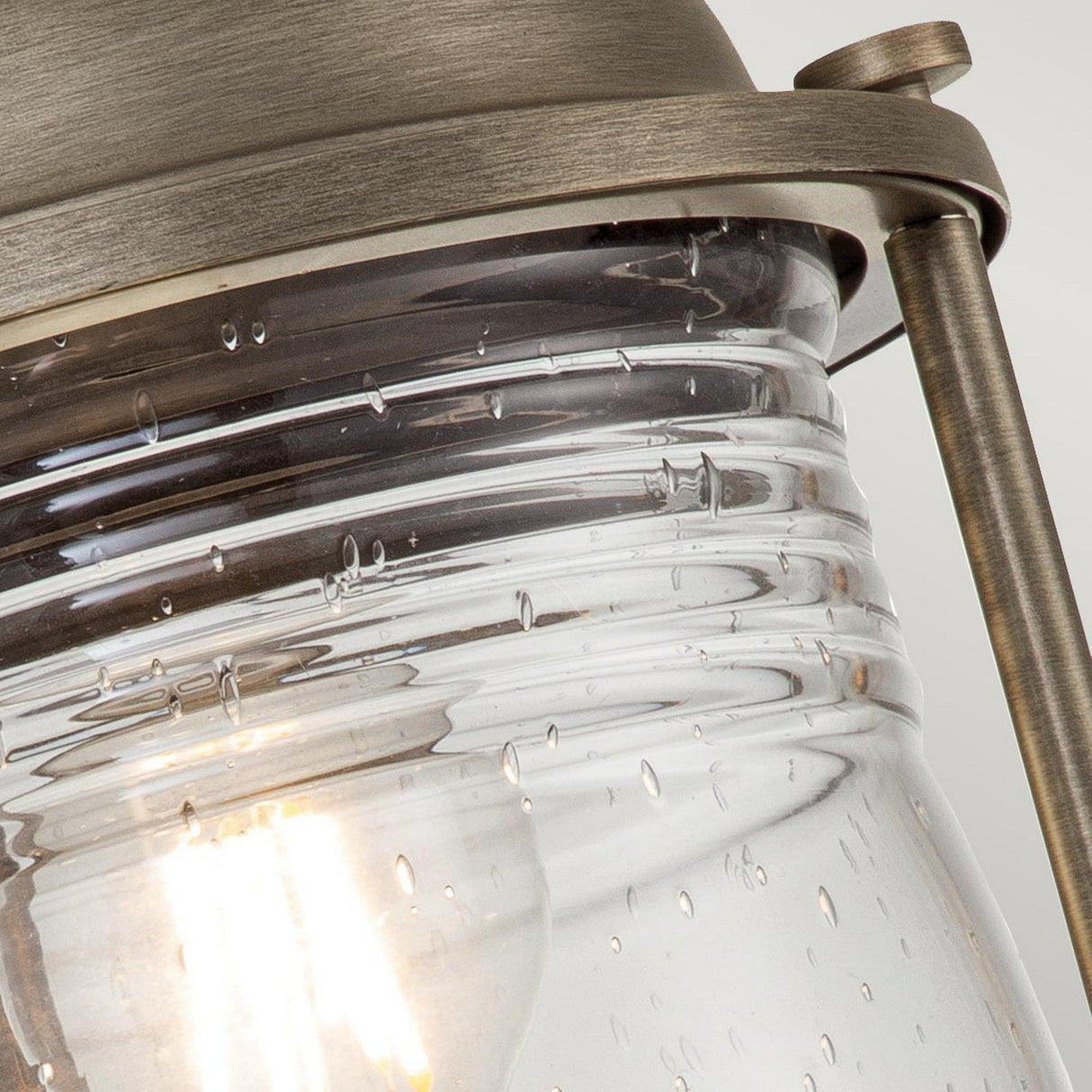 Close-up of the Ashland Bay Outdoor 1 Light Medium Pedestal Lantern in a burnished bronze finish. The lantern features textured, bubble-like glass and houses an LED Edison bulb that softly illuminates the area, enhancing its vintage aesthetic.