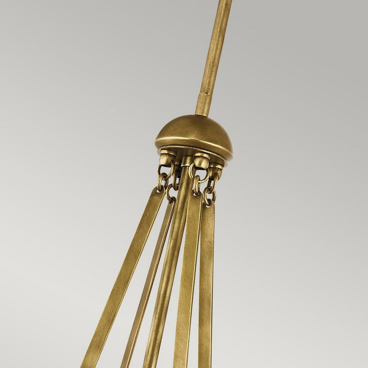 A close-up of the Aster 3 Light Pendant - Brass reveals its chandelier with long, straight arms and ribbed glass domes, each hanging by small chains from a central dome, all finished in a brass color. The plain light gray background enhances its modern elegance.