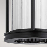 Close-up of the Barras Outdoor 1 Light Medium Wall Lantern, featuring a cylindrical ribbed glass body encased in a matte black metal frame. The clear glass enhances the lantern's sleek and contemporary design.