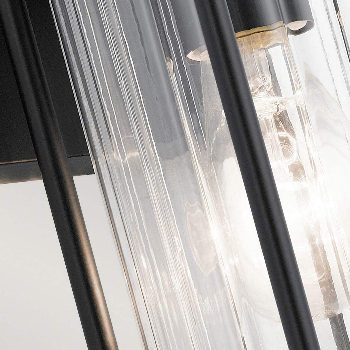 The Barras Outdoor 1 Light Small Wall Lantern in black features a sleek, modern design with a clear glass cylindrical cover and a visible light bulb, complemented by black metal rods that exude vintage charm and timeless allure.