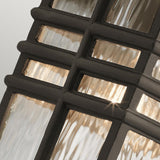 Close-up of the Beacon Square Outdoor 1 Light Medium Wall Lantern in bronze, showcasing its geometric, grid-like metal frame with textured glass panels. The warm light shines through the glass, creating a soft glow and highlighting the intricate design. The lantern is durable and weather-resistant with its IP44 rating.