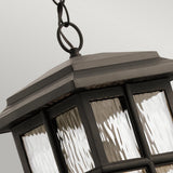 A close-up of the Beacon Square Outdoor 1 Light Chain Lantern - Bronze shows its textured glass panels gleaming atop a neutral backdrop. The lantern's dark metal frame and bronze finish create an elegant display as it hangs gracefully from a simple chain.