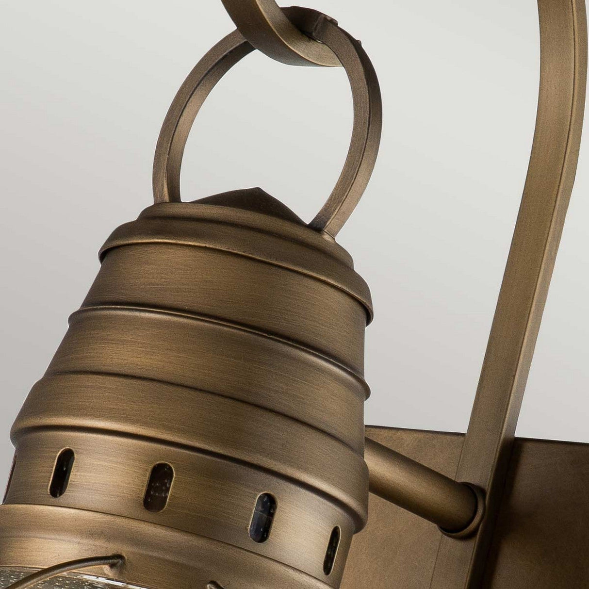 Close-up of the Bridgepoint Outdoor 1 Light Large Wall Lantern in natural brass, featuring a layered, cylindrical design and a decorative loop at the top. This lantern is reminiscent of nautical lighting and is mounted against a plain background, blending elegance with functionality.