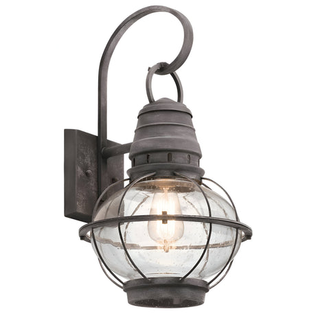 Introducing the Bridgepoint Outdoor 1 Light Large Wall Lantern in Weathered Zinc: This rustic wall-mounted lighting fixture features a glass globe encased in a protective metal cage and a decorative arm with a hook at the top.
