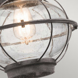 Close-up of the Bridgepoint Outdoor 1 Light Large Wall Lantern - Weathered Zinc featuring a vintage-style light bulb inside a black metal cage. The speckled, rain-like glass and weathered zinc finish enhance its charm, as the warm glow highlights the lantern's rustic design against a light gray background.