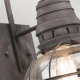 Close-up of the Bridgepoint Outdoor 1 Light Medium Wall Lantern with a weathered zinc finish. It showcases a rustic metal frame and seeded glass cover, revealing a visible bulb that emits a warm light. The finish contributes to its vintage aesthetic, enhancing its charm with an antique feel.