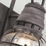 The Bridgepoint Outdoor 1 Light Small Wall Lantern showcases a rustic, industrial design with a weathered zinc metal frame and glass globe. The seeded glass presents a bubbled texture, while the light inside emits a warm glow. The fixture is secured on a metal bracket.