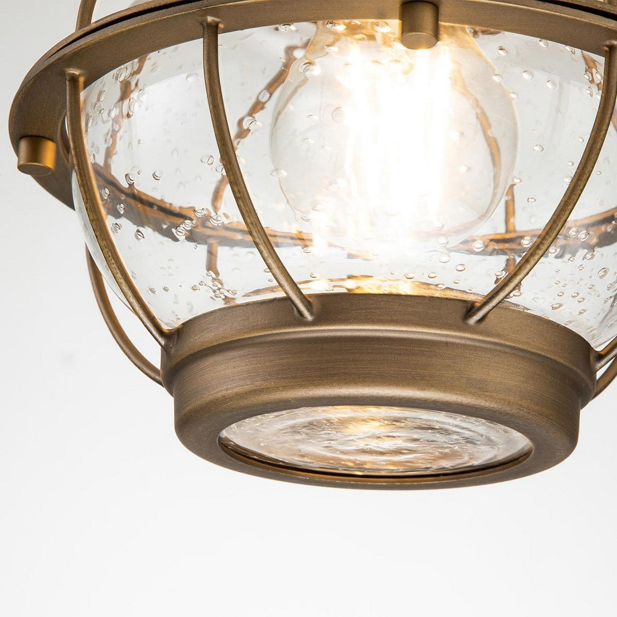 Close-up of the Bridgepoint Outdoor 1 Light Small Chain Lantern in a natural brass finish, featuring clear seeded glass with a bubble texture. The bulb inside provides a warm glow, combining industrial and modern design elements reminiscent of an outdoor lantern.