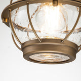 Close-up of the Bridgepoint Outdoor 1 Light Small Chain Lantern in a natural brass finish, featuring clear seeded glass with a bubble texture. The bulb inside provides a warm glow, combining industrial and modern design elements reminiscent of an outdoor lantern.