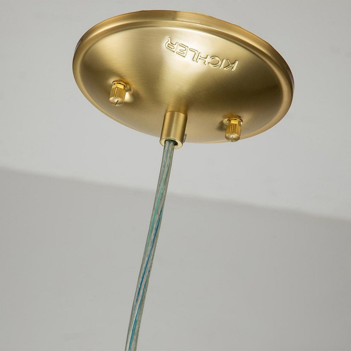 A detailed view of the Brinley 1 Light Mini Pendant, featuring a small brass fixture with a round canopy and an elegantly extending cable. This brushed brass piece from Kichler is mounted on a white ceiling, showcasing its smooth finish.