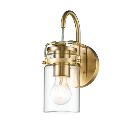 The Brinley 1 Light Wall Light in Brushed Brass features a curved arm supporting a clear glass shade that encases an exposed bulb. Its design beautifully combines modern and vintage styles, highlighted by a round brushed brass base and decorative screws, capturing the essence of vintage-inspired lighting charm.