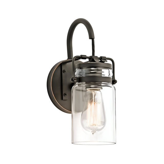 The Brinley 1 Light Wall Light - Bronze showcases a vintage design with an Edison bulb enclosed in a clear glass shade. Its rustic, dark metal finish adds to the classic appeal, while being mounted on a round bronze base enhances its industrial charm.